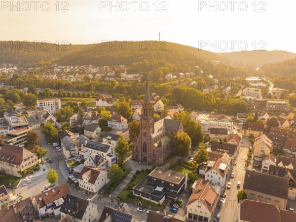Small town with central church and surrounding hills seen from above in the warm evening light,