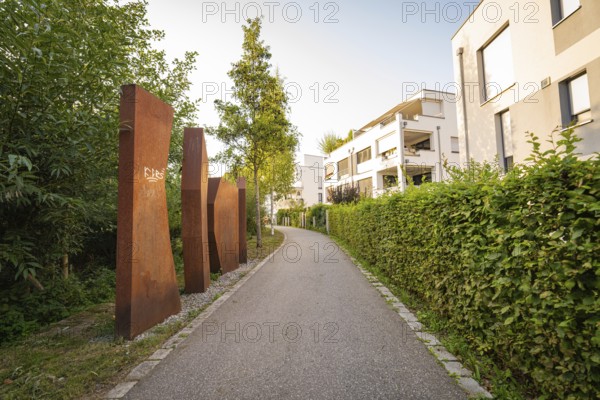 Rustic sculptures along a footpath through modern residential buildings, small town of Perle