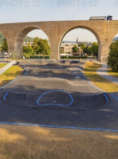 A pump track under a bridge with concrete arches and green surroundings, pump track, Nagold, Black