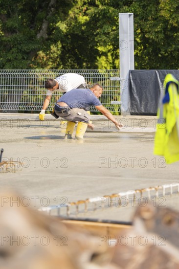 Workers bend over a concrete surface and use tools on a construction site, car park construction,
