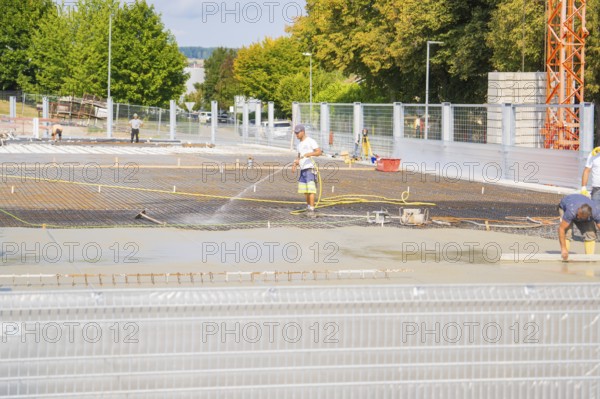 Construction workers working on the concrete surface, surrounded by trees, with safety fences, car