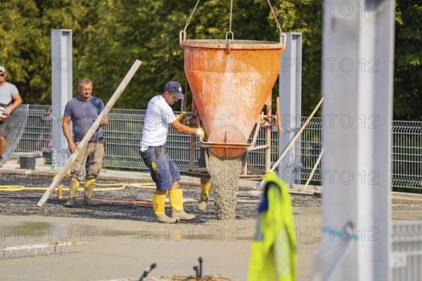 Construction workers unloading concrete with a large hopper on a building site with metal