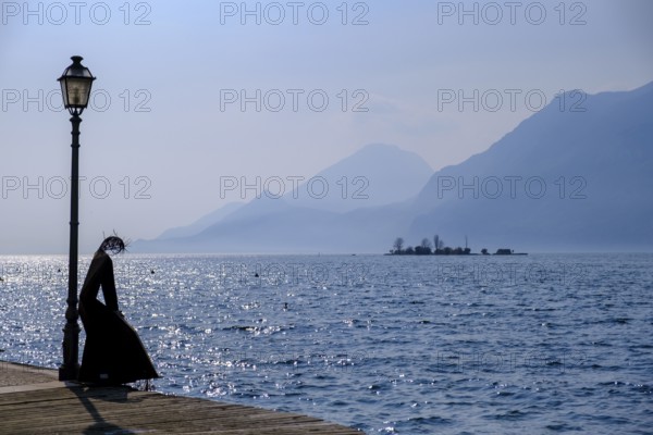 Sculpture of a fisherwoman at the harbour of Cassone di Malcesine, in the background Isole di