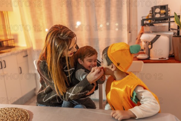 Children wearing pumpkin costumes celebrating halloween joyfully with their mother at home,