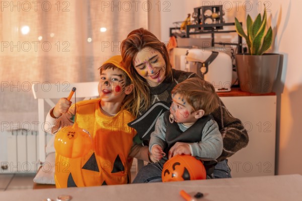 Mom and her kids are smiling, wearing halloween costumes and makeup, holding pumpkin buckets and
