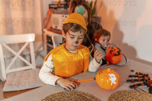 Children with painted faces preparing halloween pumpkin decorations at home, with their mother