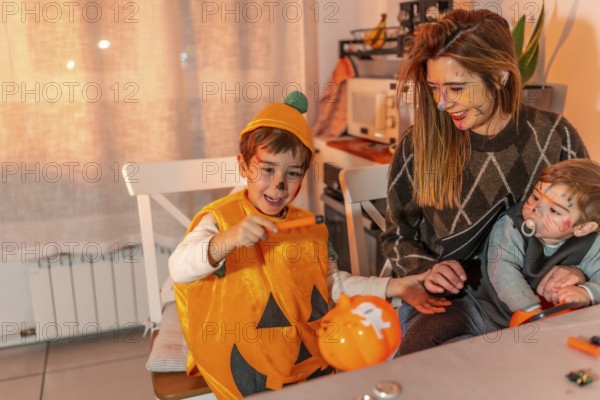 Happy children with painted faces wearing halloween costumes painting pumpkins with their mother at