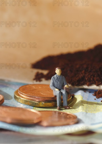 Miniature figure of a man sitting on coins and banknotes, ground coffee in a filter bag in the