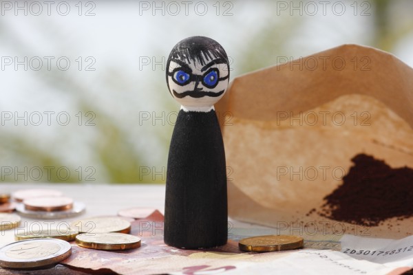 Male wooden cone figure with coins and banknote in front of filter bag with coffee North