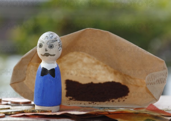Male wooden cone figure with coins and banknote in front of filter bag with coffee North