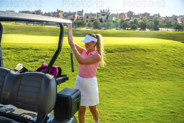 Female golfer placing her golf club into the cart while enjoying a sunny day on a lush green golf