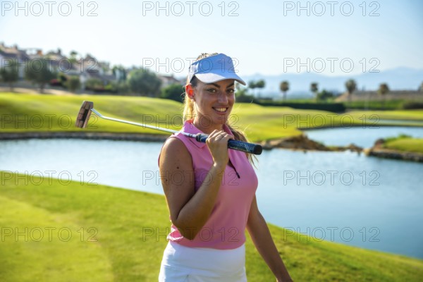 Female golfer smiling and holding her putter on shoulders on a sunny day on the golf course next to
