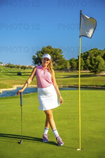 Female golfer standing confidently near the hole, holding her putter on a sunny day at the golf