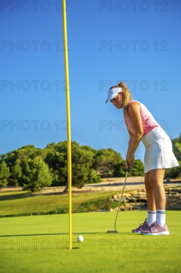 Professional golfer concentrating on the green, about to putt during a sunny day on a beautiful
