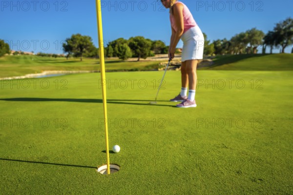 Woman skillfully putting on a golf course, aiming for the hole under a clear blue sky. Lush green