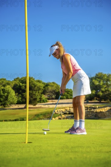 Professional golfer putting a ball on the green under the bright sun, enjoying a beautiful day on a