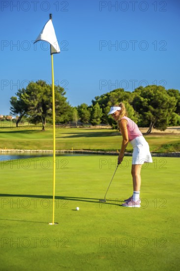 Female golf player putting the ball on the green under a bright sun, showcasing skill and