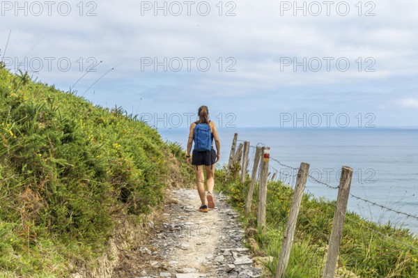 Female tourist walking along a coastal path in zumaia, basque country, enjoying the scenic view of