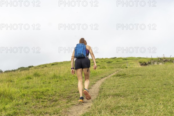 Female tourist walking up the grassy hill at sakoneta beach near zumaia in the basque country,