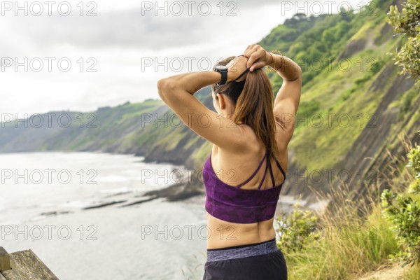 Rear view of a sportswoman tying her ponytail while enjoying the view of the sea and the flysch