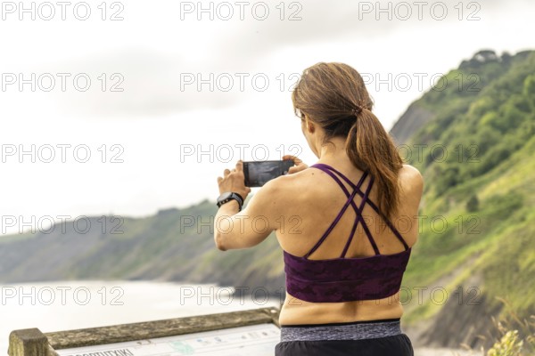 Sportswoman uses her smartphone to capture the impressive view of the flysch cliffs at sakoneta