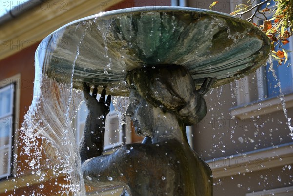 Water flowing from a basin held by a beautifully crafted statue, creating dynamic jets and splashes