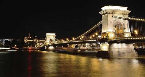 Chain bridge reflecting on danube river with gresham palace in background at night, budapest,