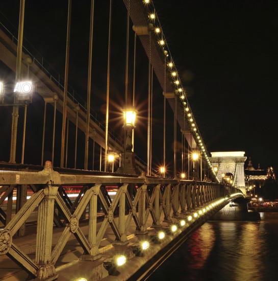 Chain bridge glowing beautifully at night, showcasing blurred car light trails against the backdrop
