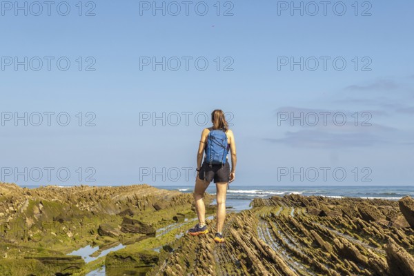 Female hiker with backpack admiring the stunning coastal rock formations of the zumaia flysch on