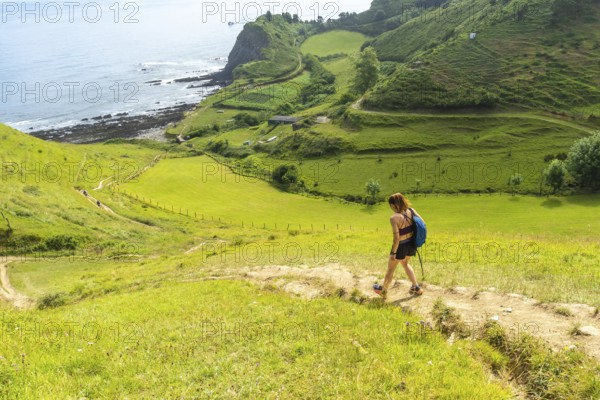 Female hiker walking down a path in the hills near sakoneta beach in zumaia, basque country, spain,