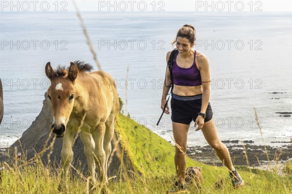 Female hiker with her dog encountering wild horses while walking on the cliffs of sakoneta beach,