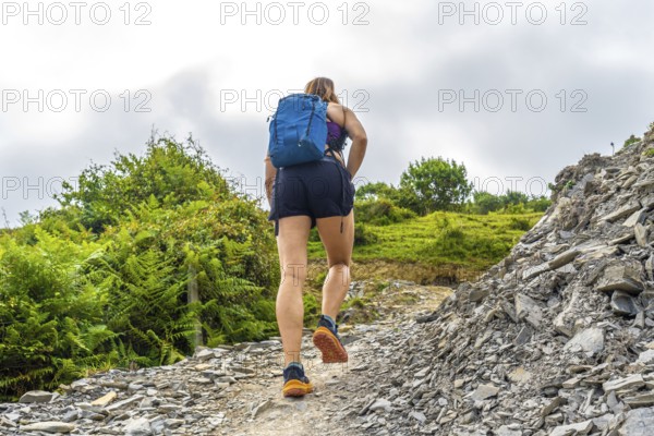 Female hiker ascending a steep, rocky trail in zumaia, basque country, showcasing the rugged beauty