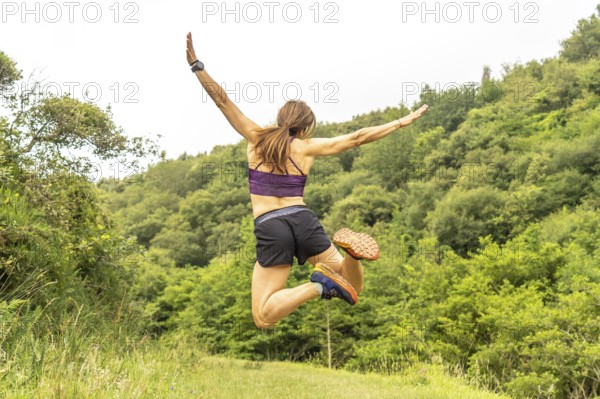 Celebrating athletic achievement, a woman jumps with outstretched arms amidst the verdant hills