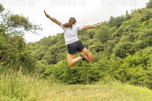 Celebrating athletic achievement, a female athlete jumps with outstretched arms in a vibrant green