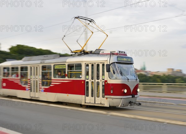 Red and white tram carrying passengers is crossing a bridge in prague, czech republic, providing