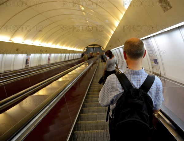 Tourist with a backpack ascending an escalator in a bustling subway station, surrounded by urban