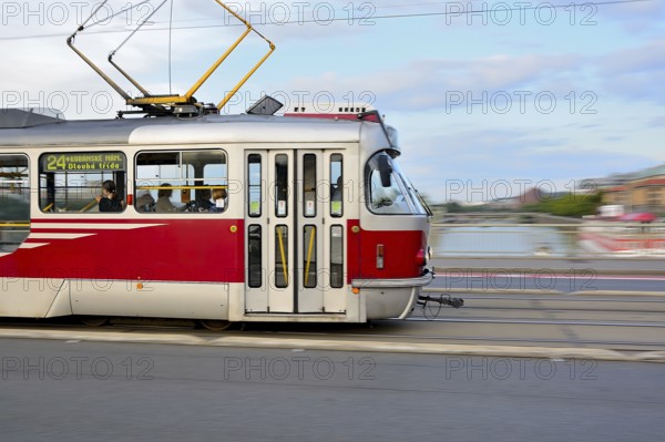 Red and white tram crossing a bridge in prague, creating a dynamic motion blur over the vltava