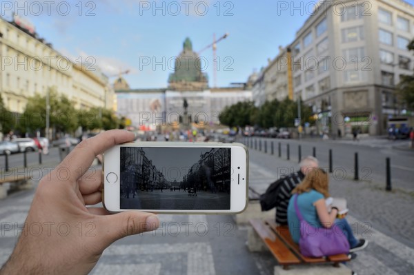 Hand holding smartphone taking photo of wenceslas square in prague, czech republic, with tourists