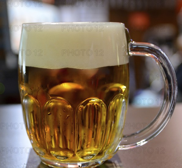 Large glass mug full of cold, golden beer with a thick head, creating a refreshing scene in a pub,