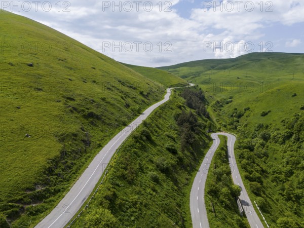 Serpentine road winding through green hills under partly cloudy sky, aerial view, road H52 above a