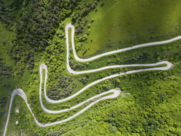 Serpentine road winding through green hills and forests, aerial view, road H52 above a tunnel,