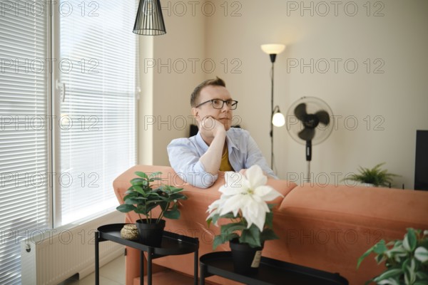 A man sits thoughtfully on a couch in a cozy living room, enjoying a moment of reflection. Bright