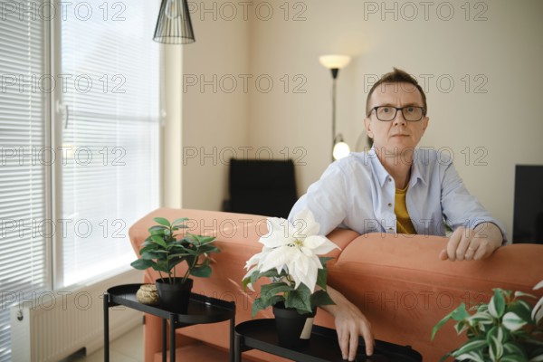 A middle-aged man sits on an orange couch in a contemporary living room. He appears thoughtful as