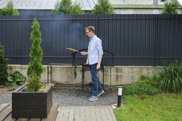 In a vibrant backyard garden, a man stands next to a grill, skillfully cooking skewered food. Lush