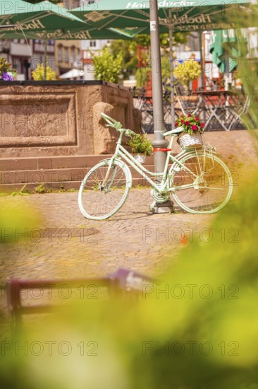 A white bicycle stands decoratively in front of a fountain in the town, small town of Perle Calw,