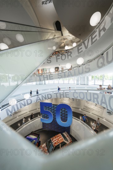 Interior of an exhibition decorated with a curved staircase and large numbers, BMW Welt, Munich,