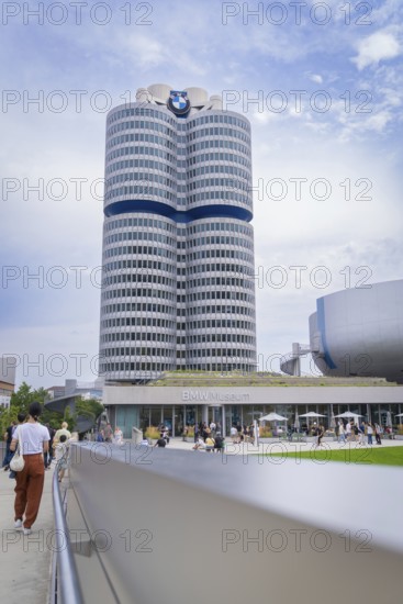 High-rise building next to a modern round building, visited by many people under a partly cloudy