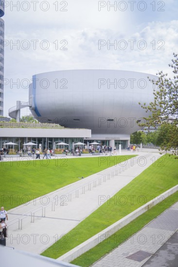 Large modern building surrounded by a green park with people out for a walk, BMW Welt, Munich,