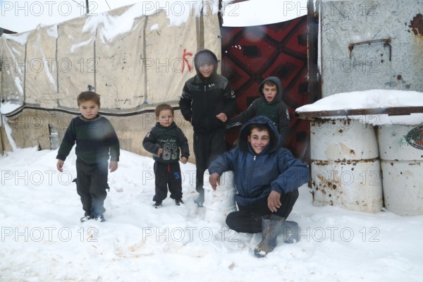 Displaced Syrian children playing in the snow near their tents inside a refugee camp during winter.