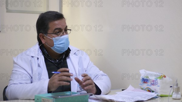 A Syrian doctor wearing a protective mask consults with a displaced patient inside a medical clinic